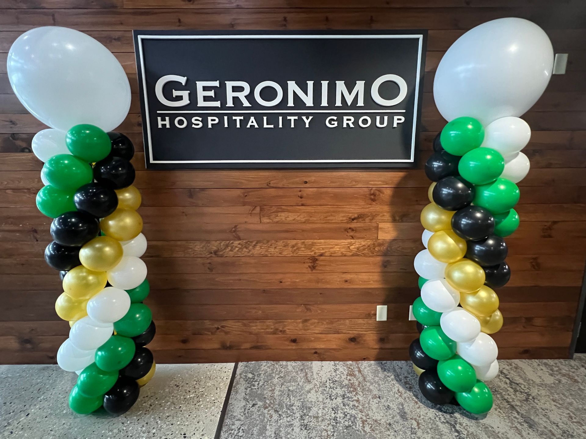 Two columns of balloons in front of a sign for geronimo hospitality group