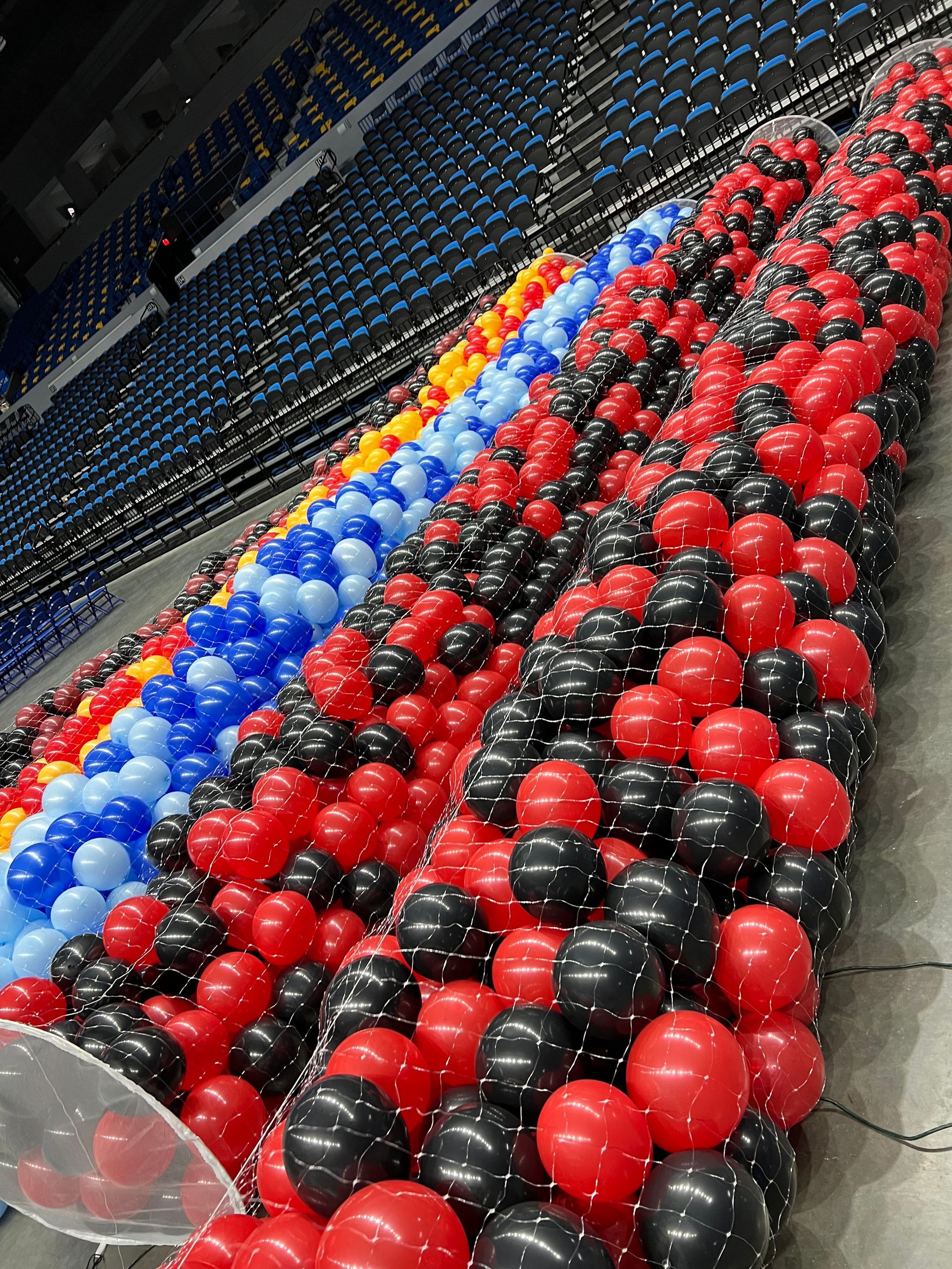A bunch of red , black and blue balloons in a stadium
