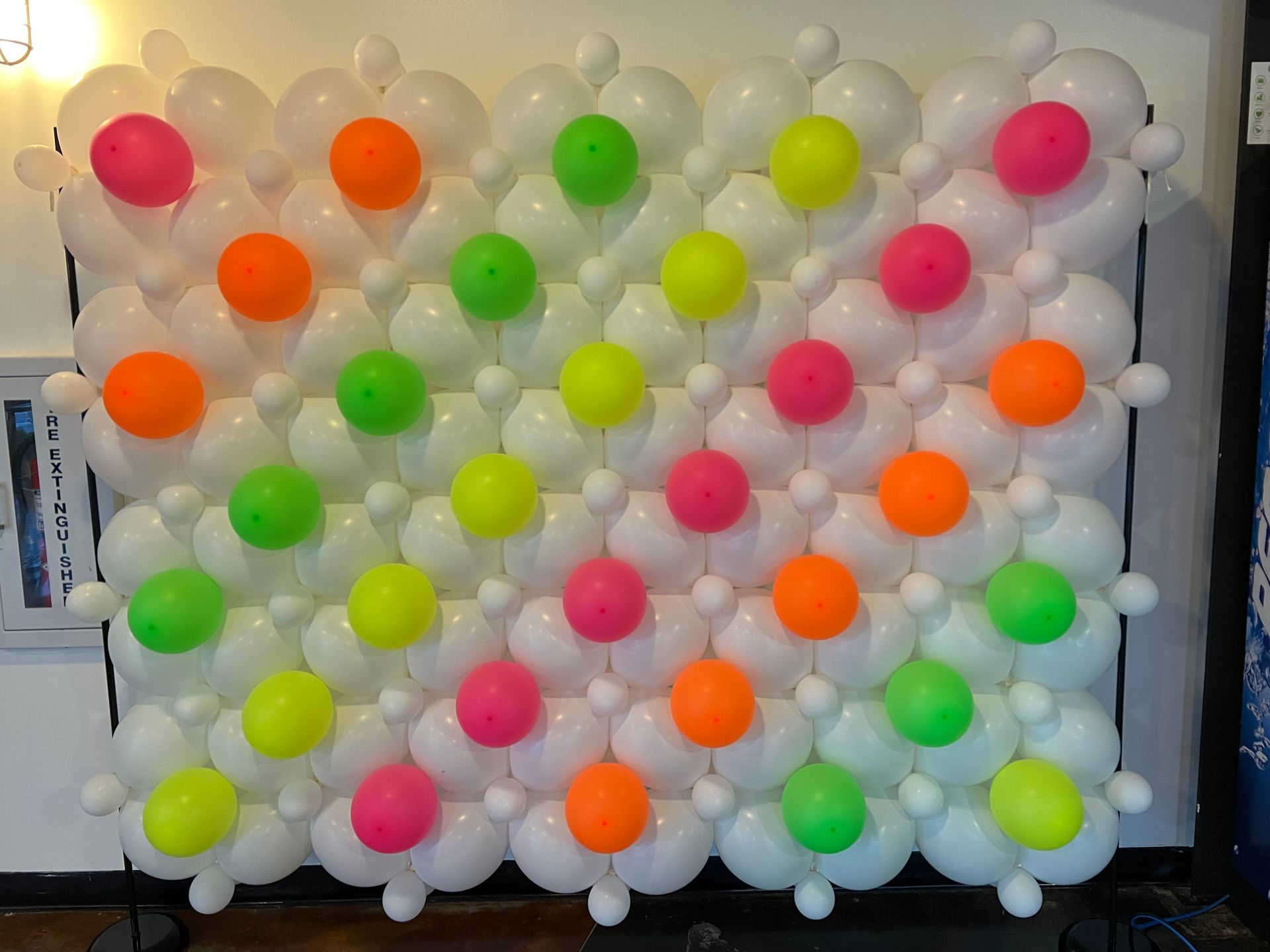 A wall made of white balloons and neon colored balloons