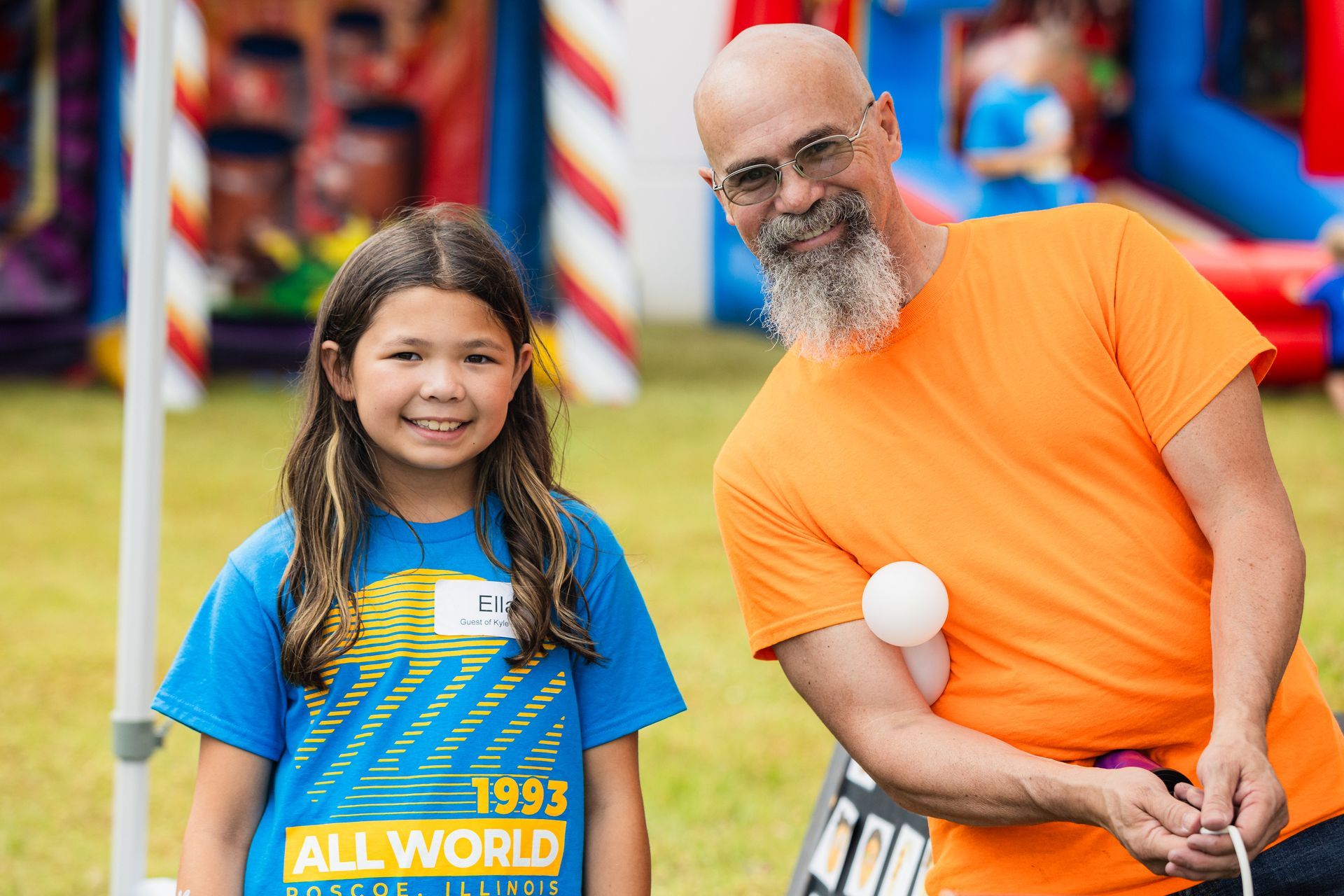 A man and a girl are standing next to each other in front of a bouncy house.