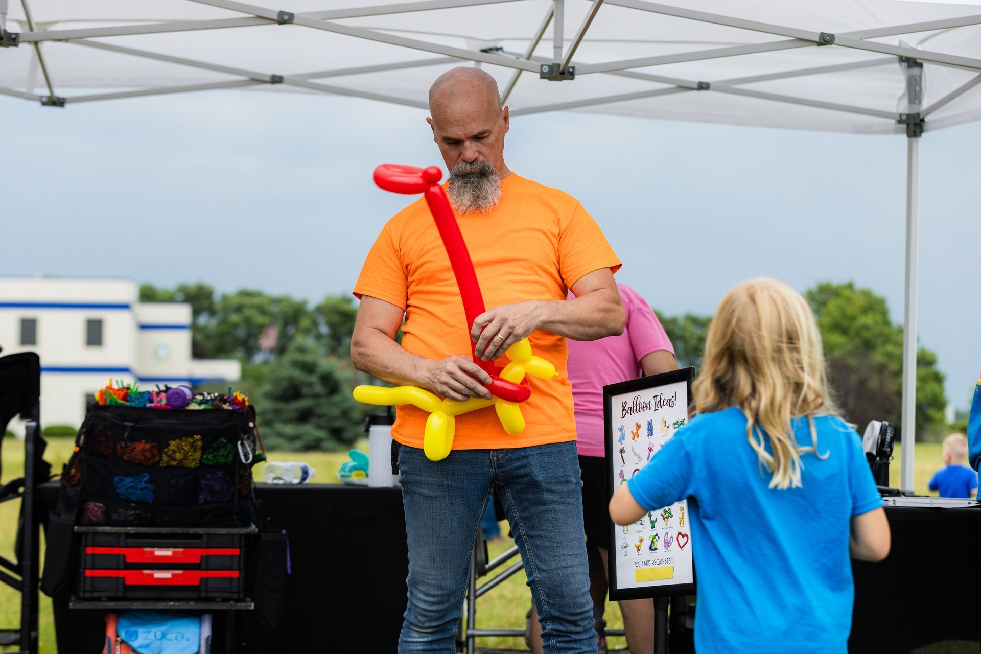 A man is making a balloon animal while a little girl watches.