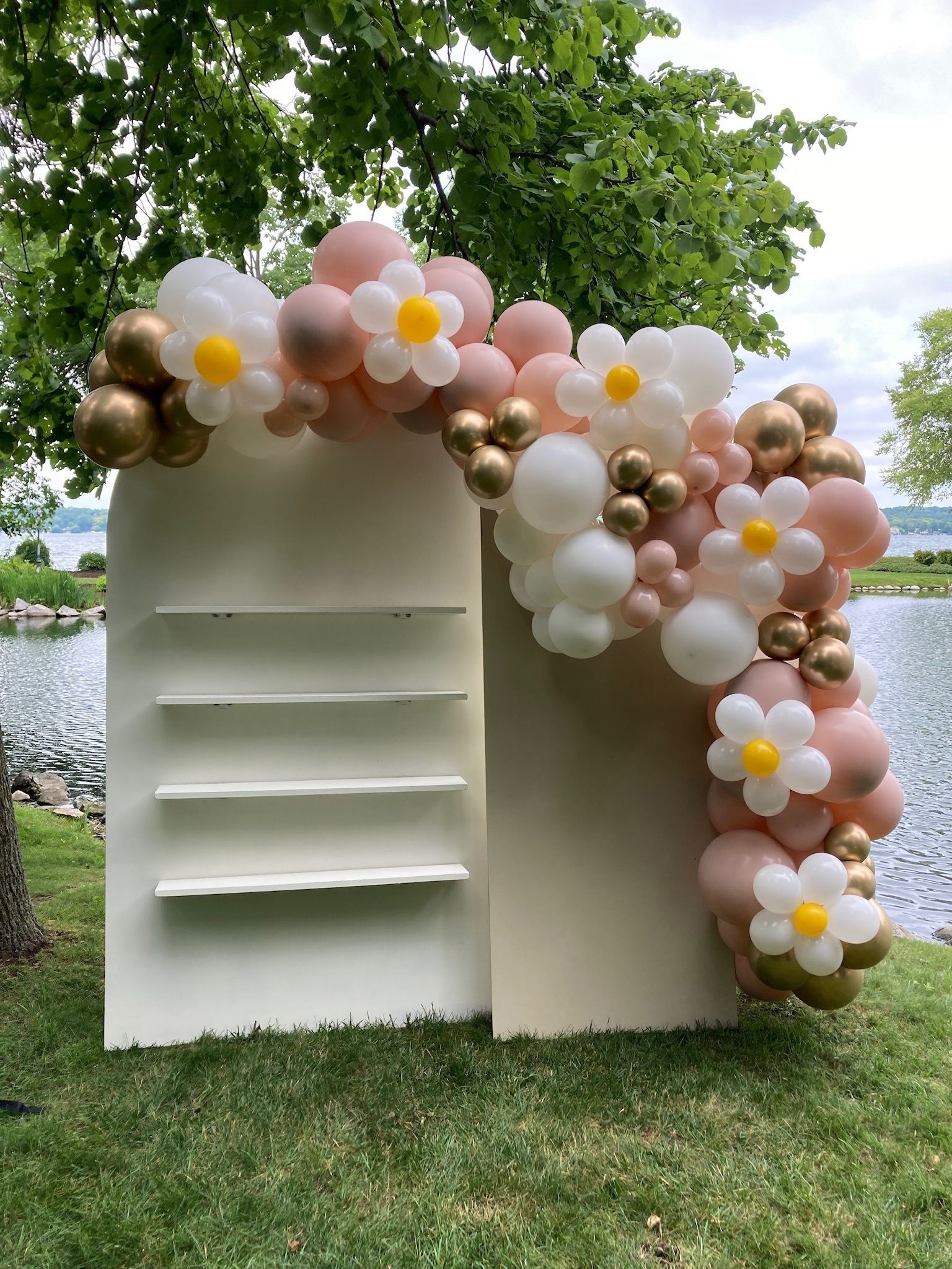 A white wall with balloons and flowers on it is sitting on top of a lush green field.