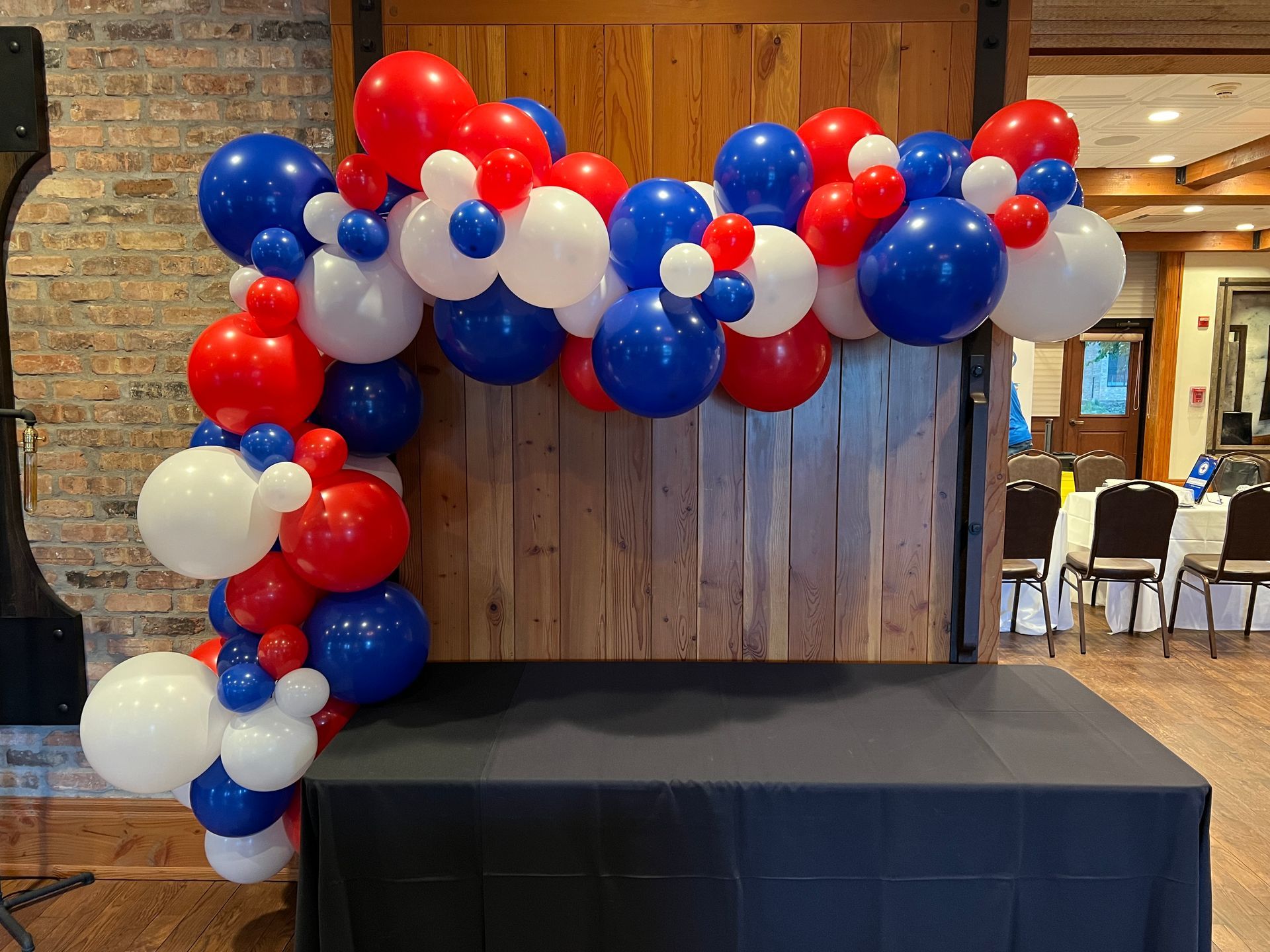 A table with a red , white and blue balloon arch behind it.
