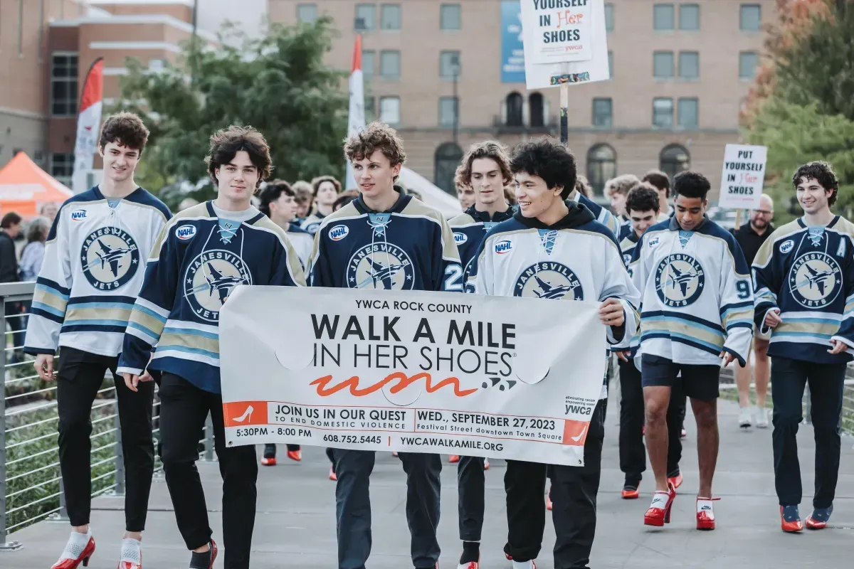A group of young men are holding a sign that says `` walk a mile in her shoes ''.