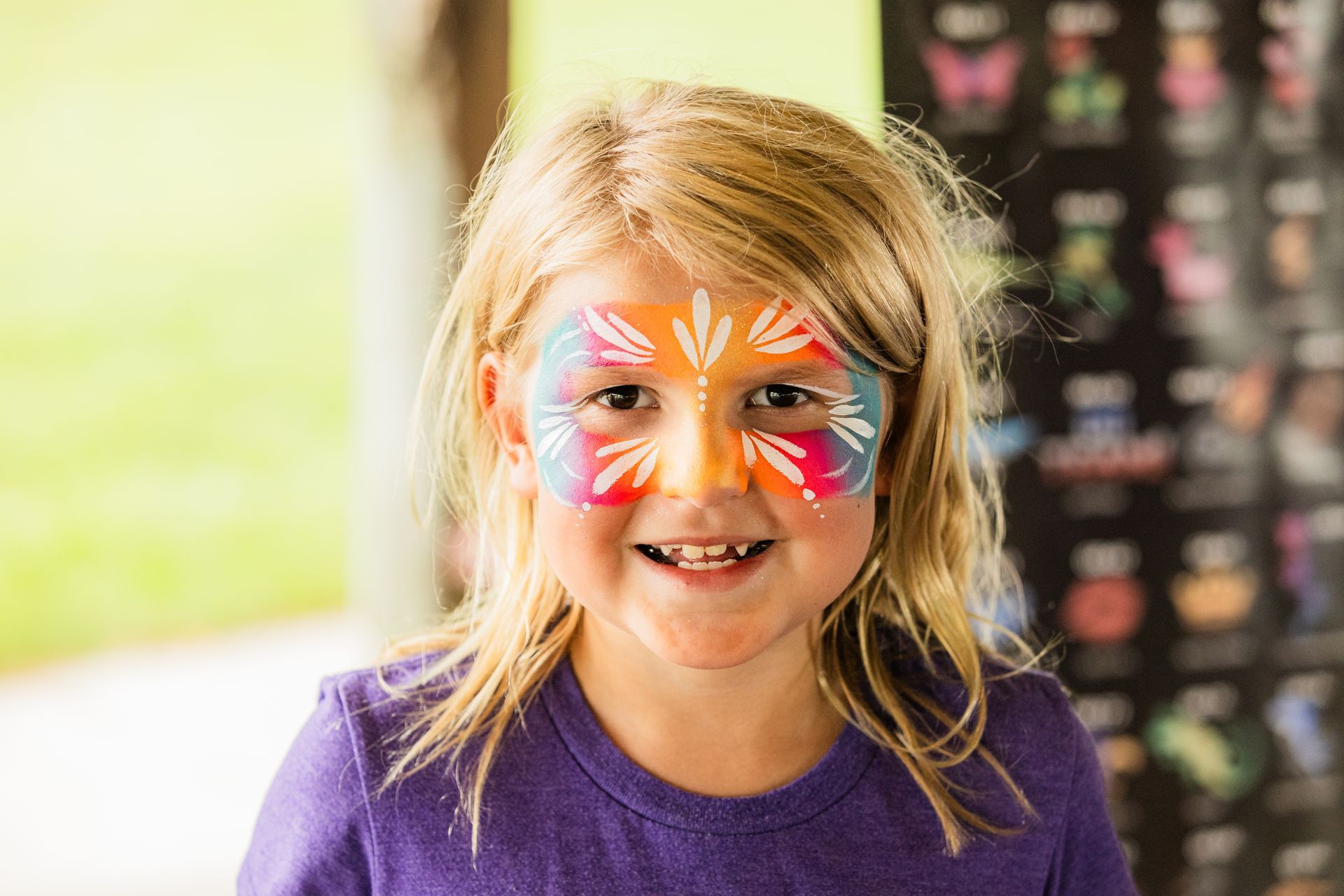 A little girl with her face painted in a colorful design.