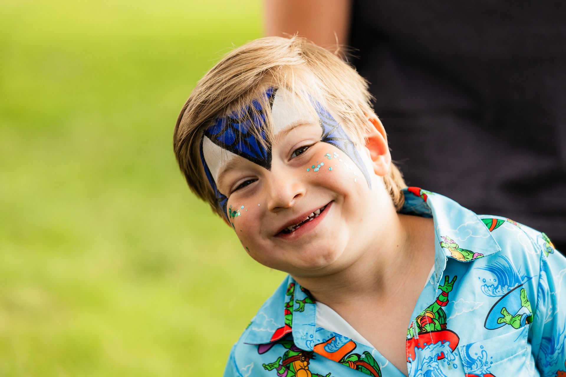 A young boy with face paint on his face is smiling.