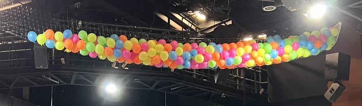 A bunch of colorful balloons are hanging from the ceiling of a stage.