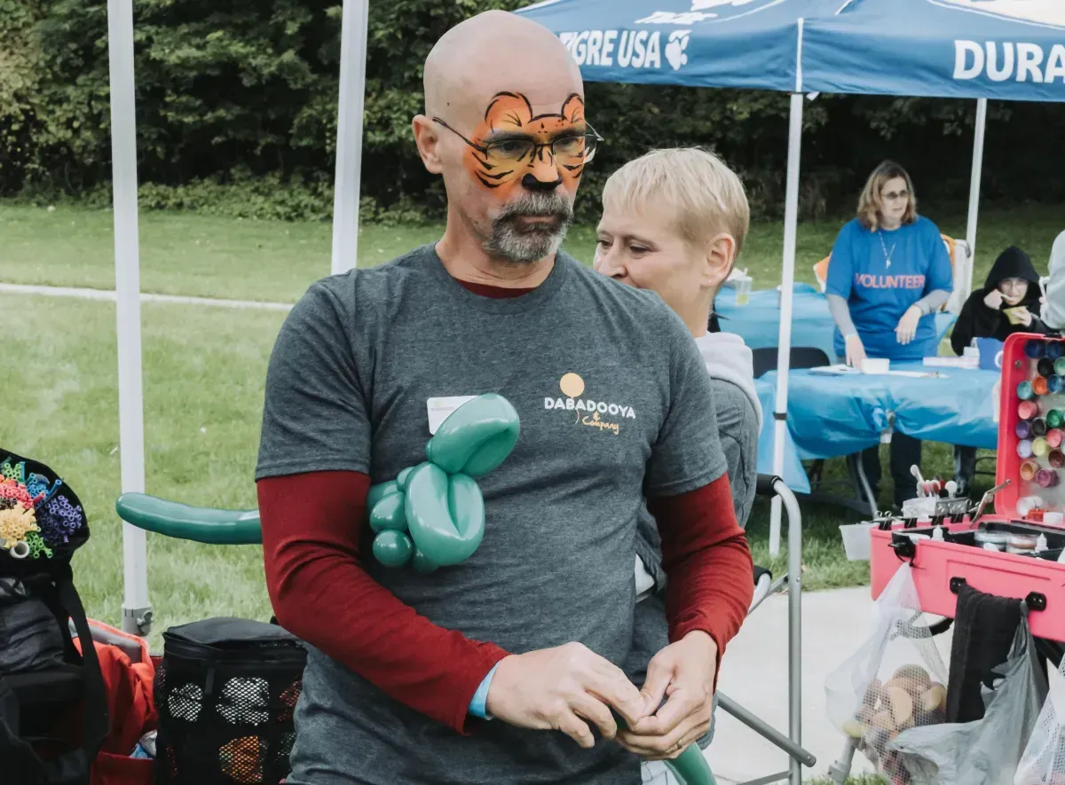 A man with a cat face painted on his face is holding a balloon.