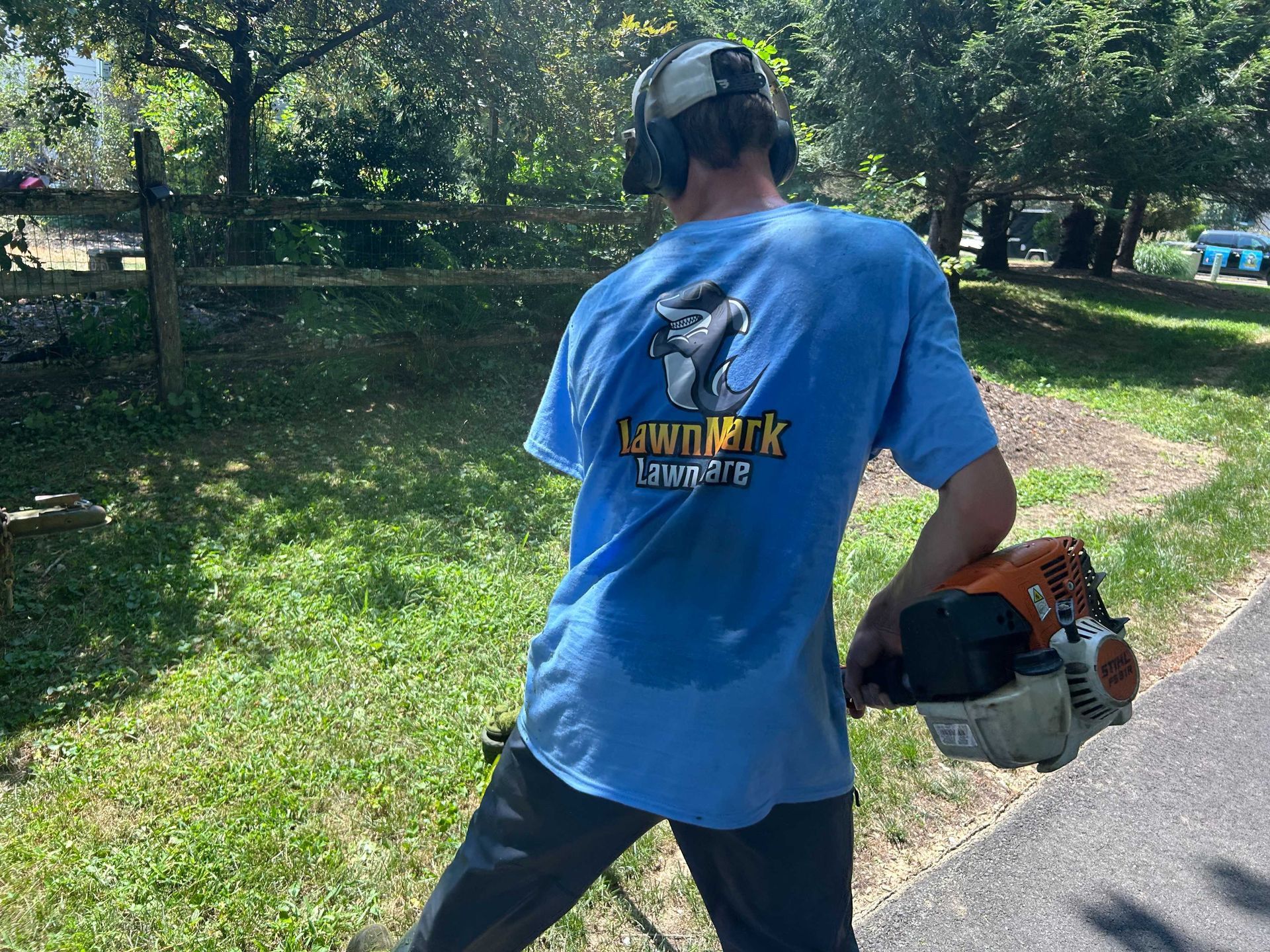 Person using a string trimmer to cut grass; outdoors on a sunny day.