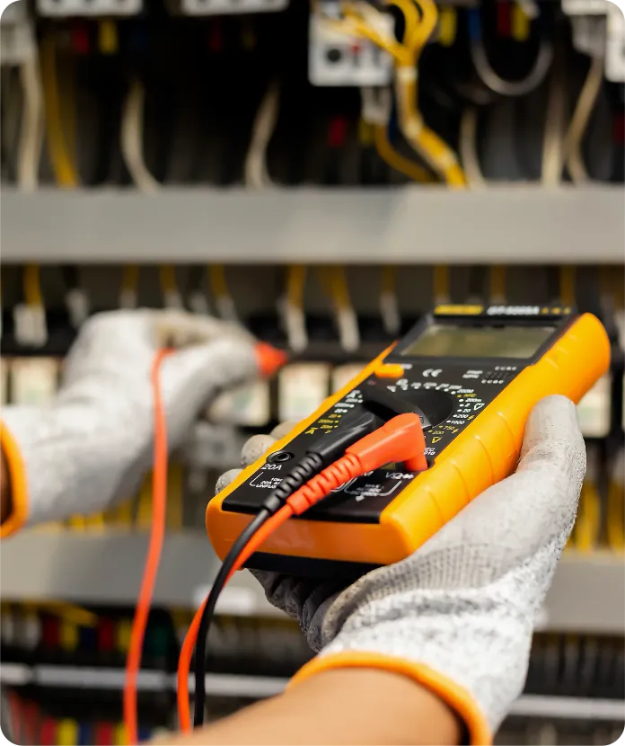 Electrician testing wires with a multimeter in a control panel, wearing gloves.