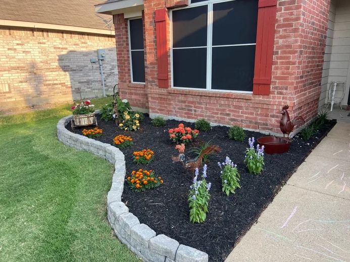Brick house with flower bed edged with grey blocks. Dark mulch and colorful flowers.