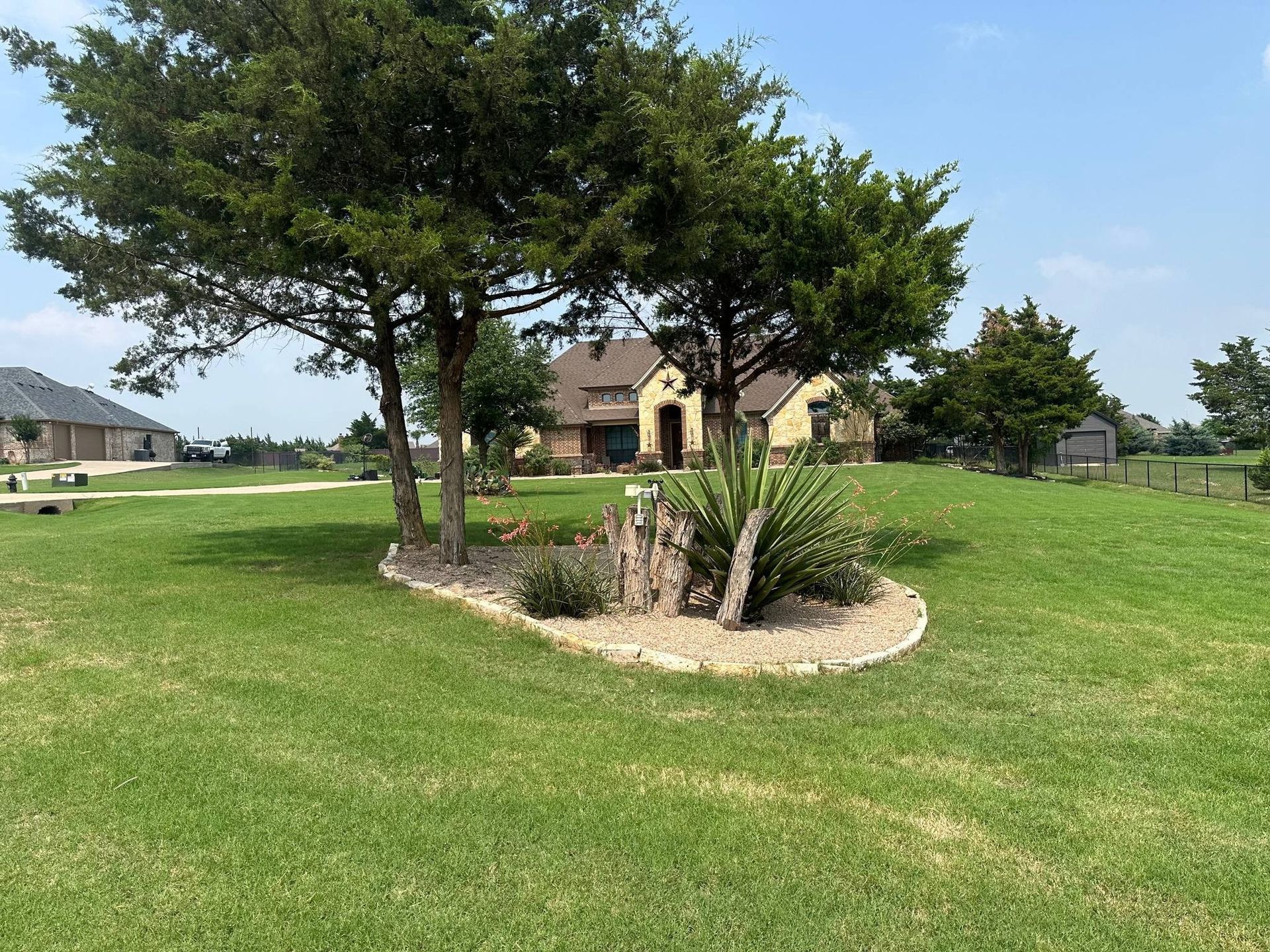 Green lawn with a house in the background and a rock garden with trees in the foreground.