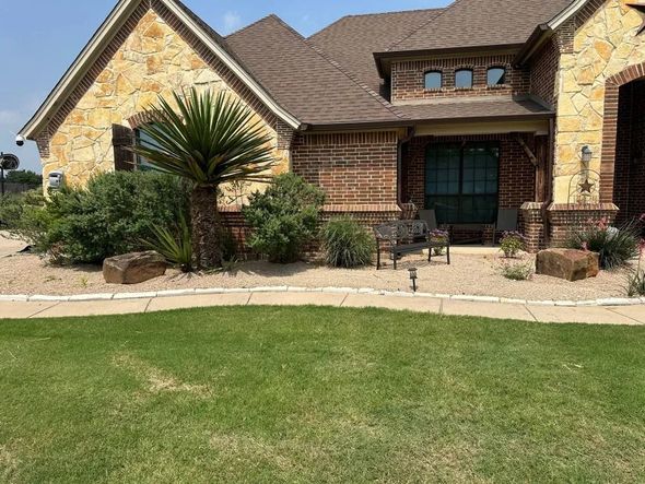 House exterior with stone and brick facade, lush lawn, and desert landscaping.