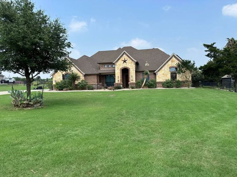 Single-story house with brown roof, stone facade, star decor, and green lawn under a blue sky.