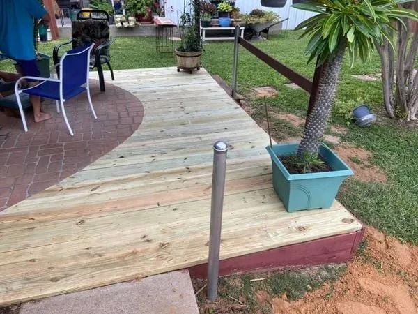 Wooden deck with a potted palm tree, leading to a brick patio. Person in blue shirt.