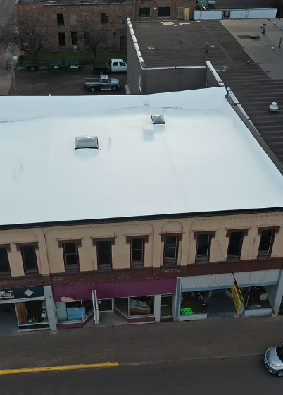 Overhead view of a downtown building with a bright white roof, beige facade, and storefronts below a street.
