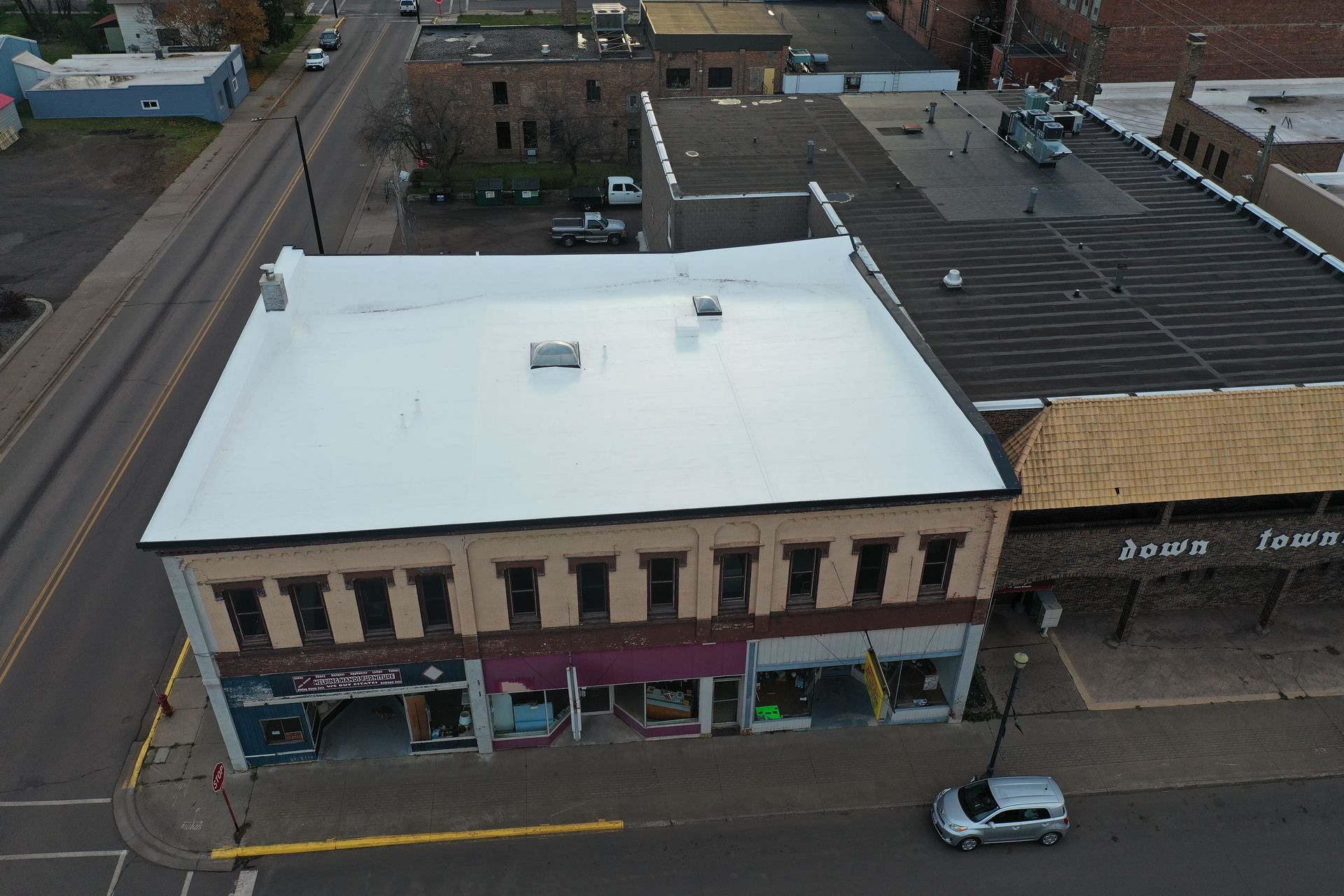 Aerial view of a two-story brick building with a white roof on a city street, shops below.