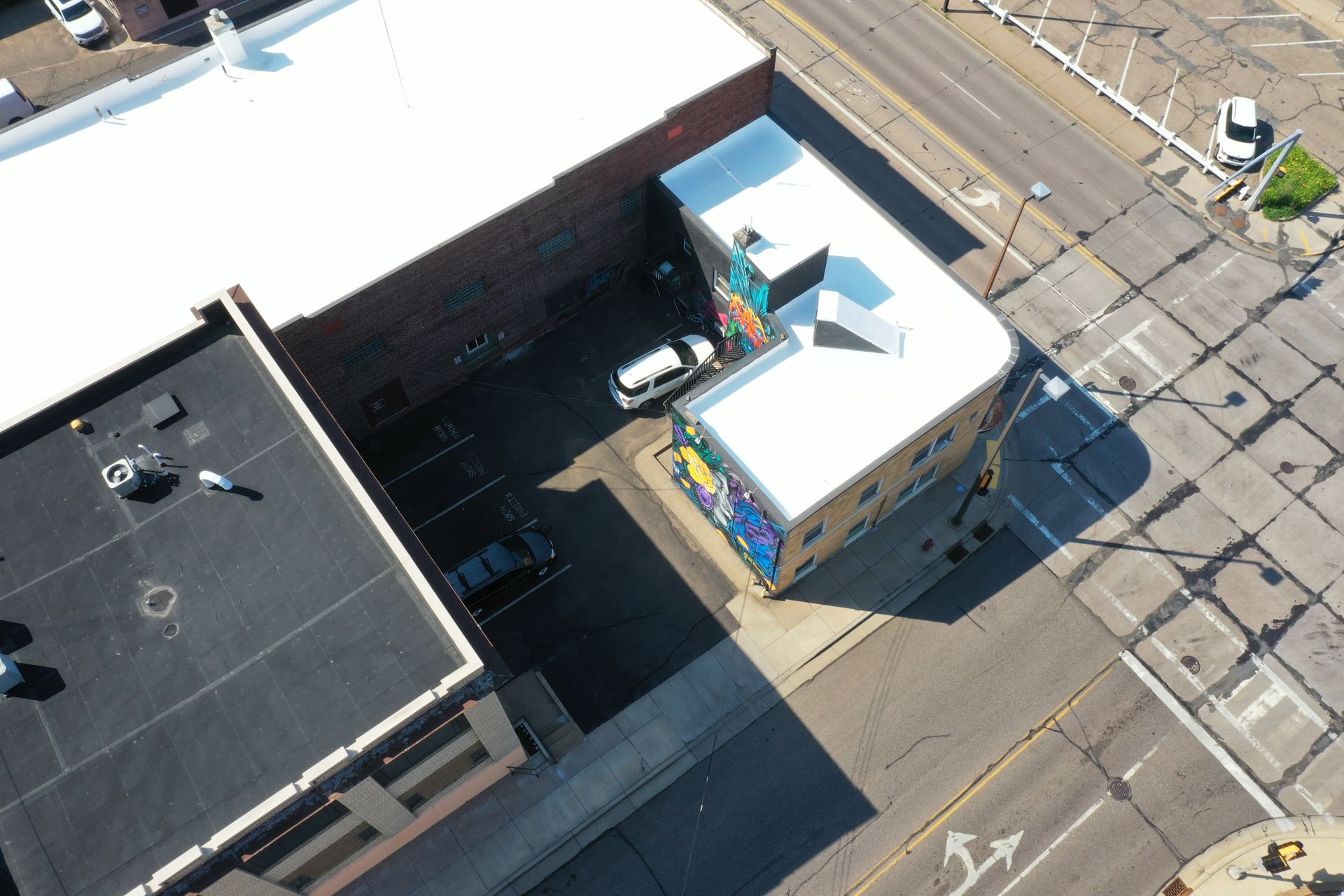 Aerial view of brick buildings, parking area with cars, and a street corner.