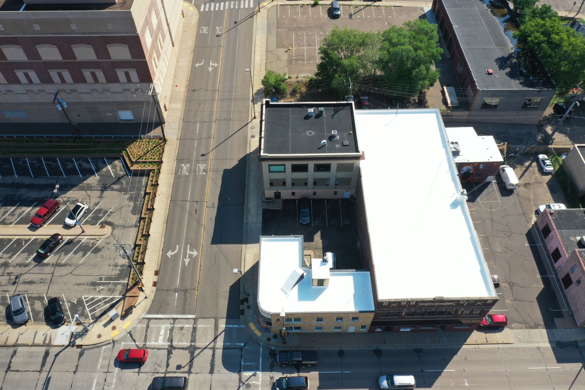 Aerial view of city buildings and a street. Cars and trees are visible.