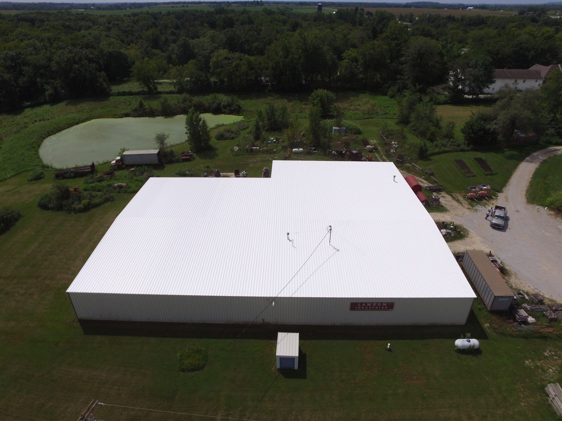 Aerial view of a large white industrial building surrounded by green grass and trees.