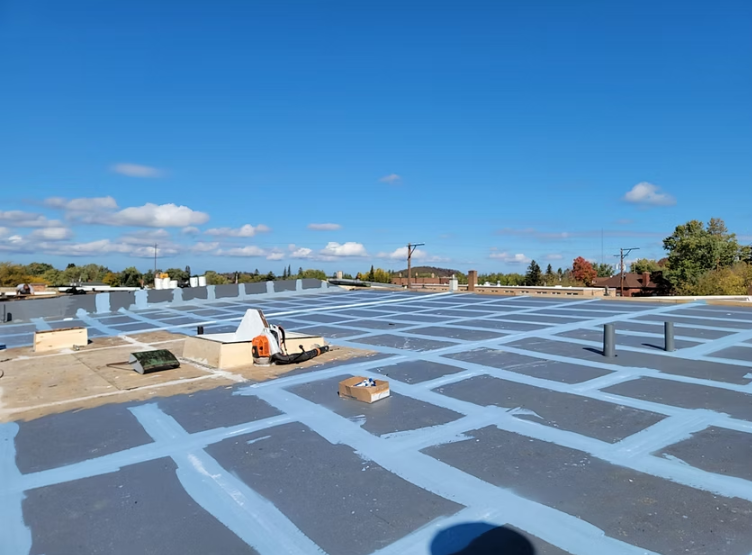 A flat commercial roof with a blue sky; workers are installing a roofing system.