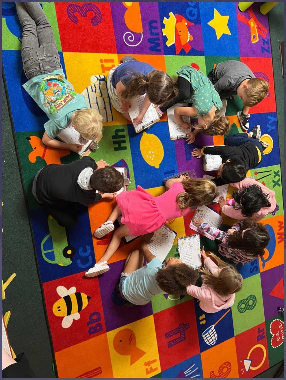 A group of children are laying on a colorful rug reading books.