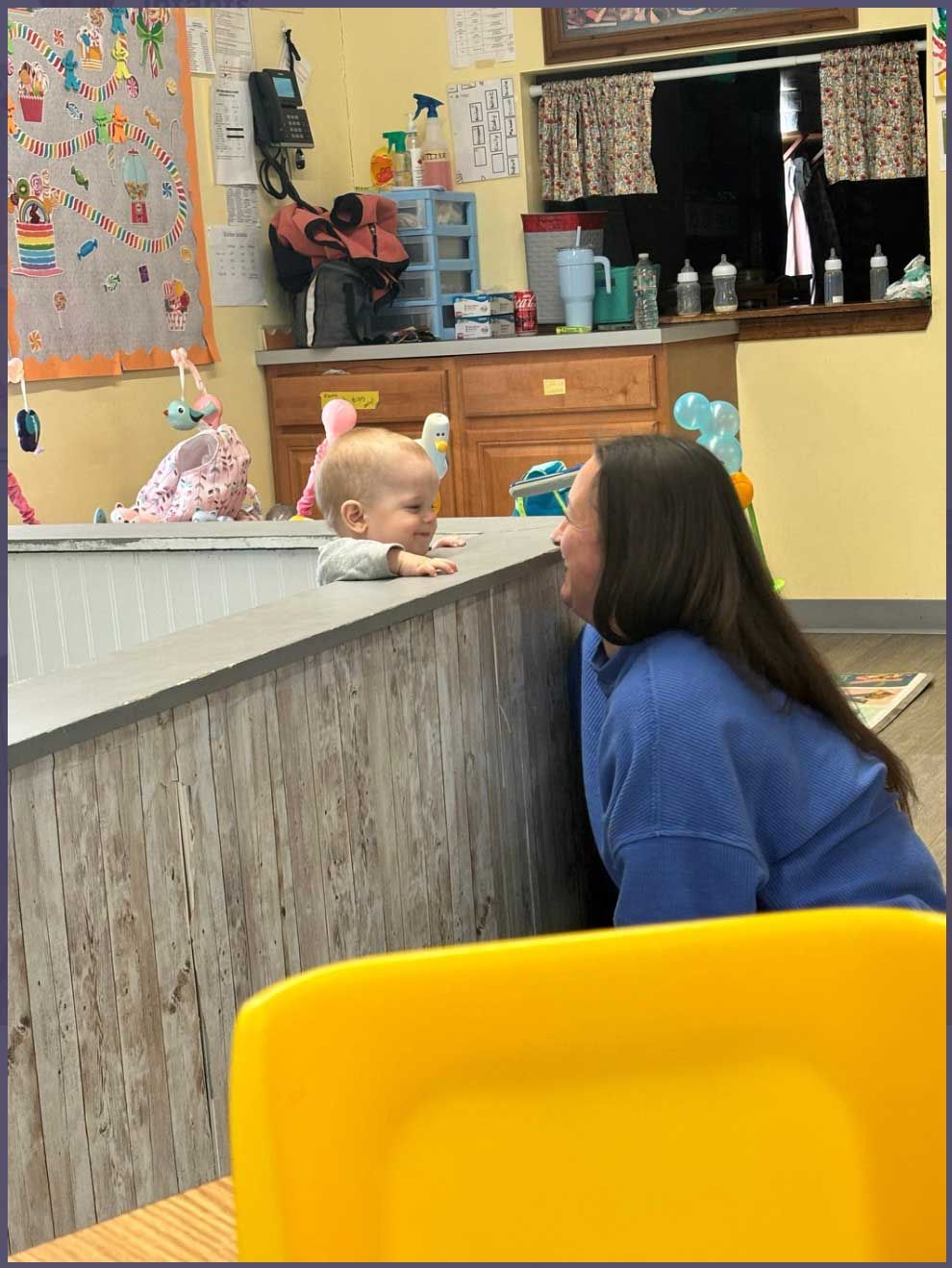 A woman is sitting in a yellow chair talking to a baby.