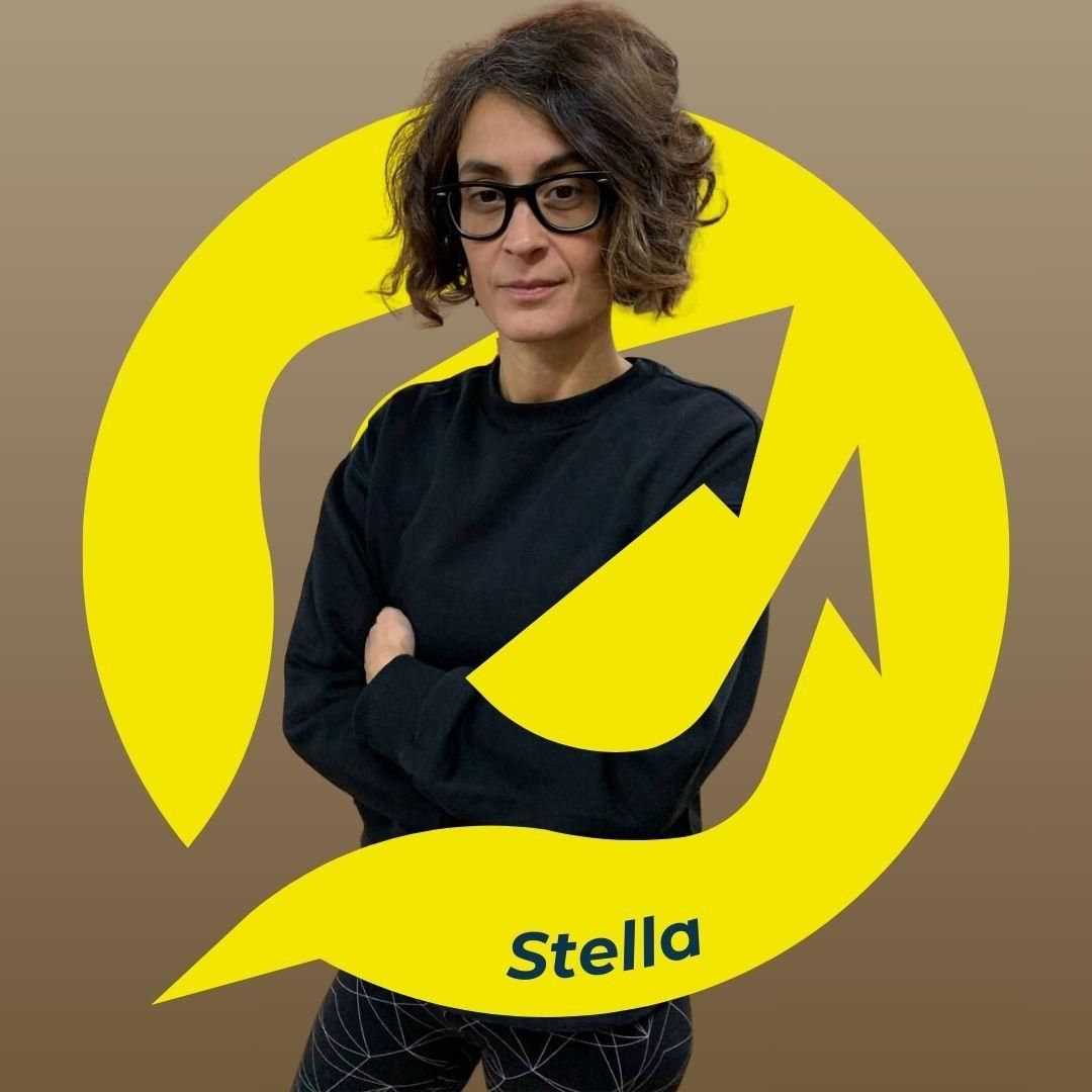 Una donna di nome Stella, con le braccia incrociate, indossa occhiali e abiti neri, all'interno di un logo giallo.