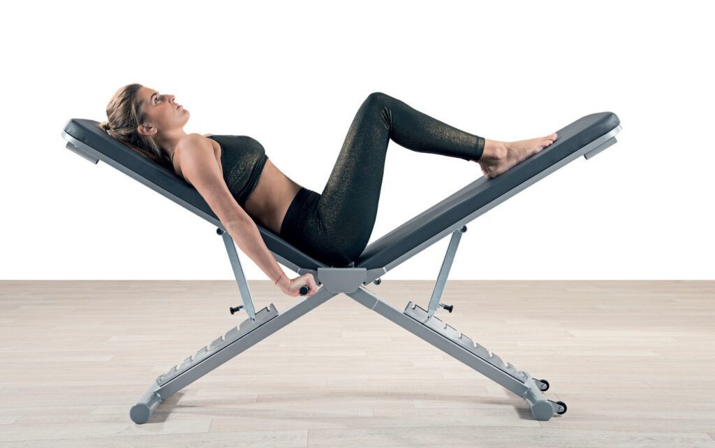 Donna sdraiata su una panca inclinata, intenta a fare esercizi addominali. Abito nero, ambiente luminoso.