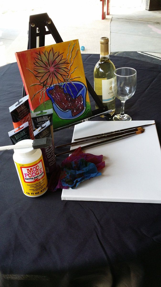 Art supplies, wine, and a painting in progress on a table.