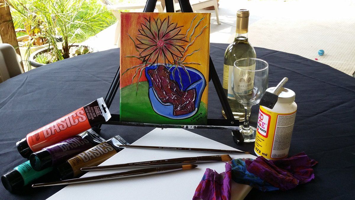 Art supplies and wine on a table: painting, brushes, paints, canvas, wine bottle and glass.