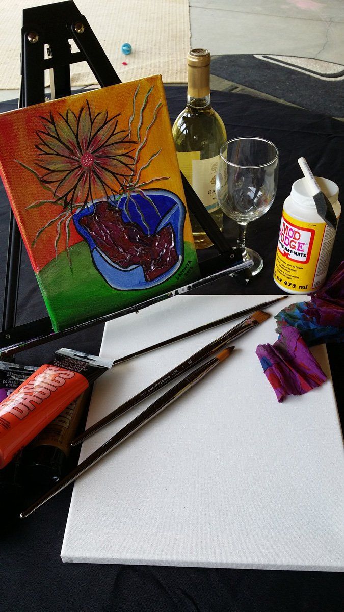 Painting supplies: canvas, brushes, paint, wine bottle and glass, and a finished painting.