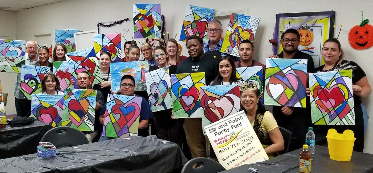 Group of people holding colorful heart paintings, smiles in a room.