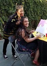 Woman in bee costume poses next to another woman painting outdoors.
