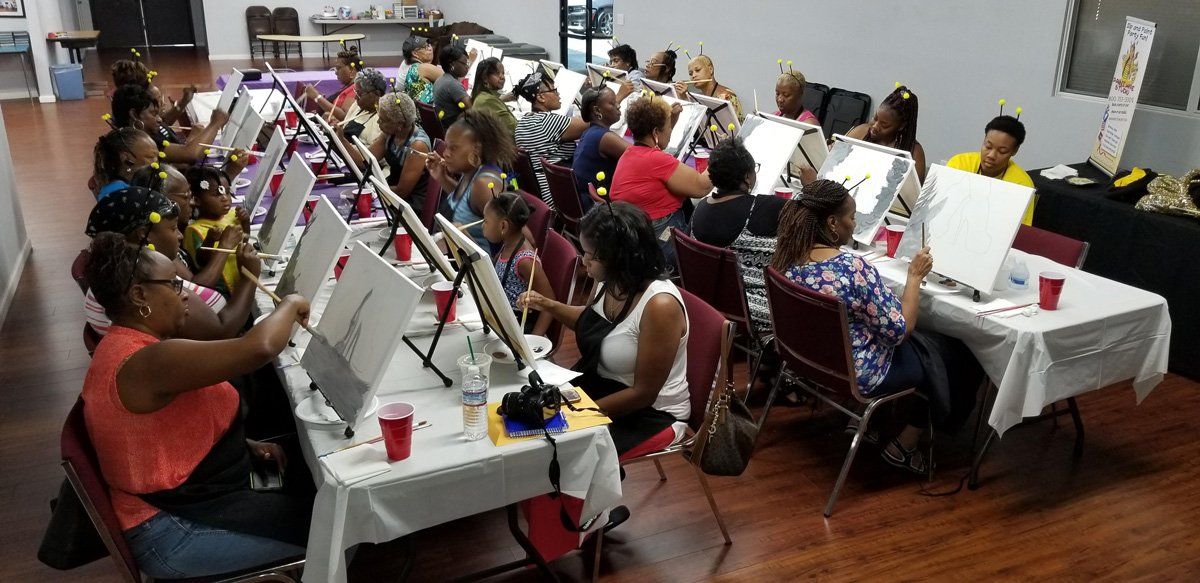People painting at tables in a room, some holding up their canvases.