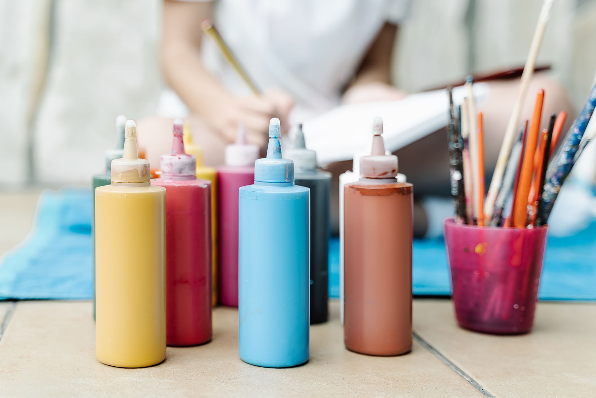 An easel with a blank canvas, wine bottle, paint, brushes, and a glass on a table.