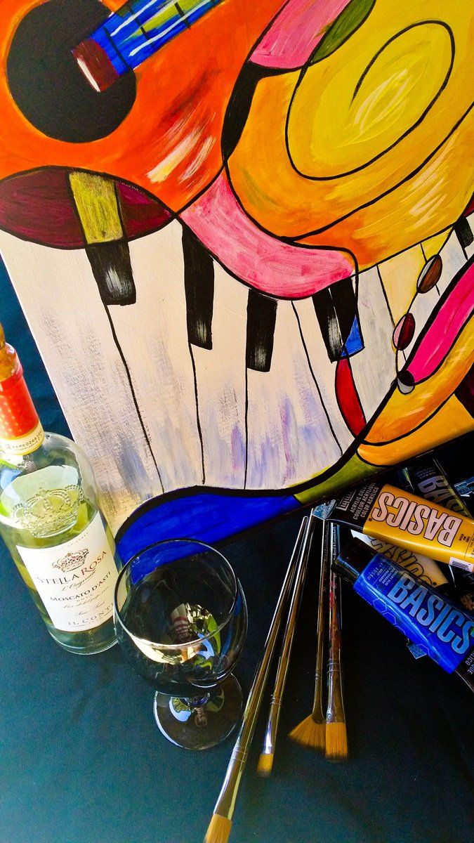 Colorful abstract painting with piano keys, paint tubes, brushes, and a glass of wine.