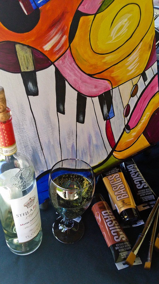 Piano-themed painting, wine bottle, glass of wine, paint tubes, and brushes on a table.