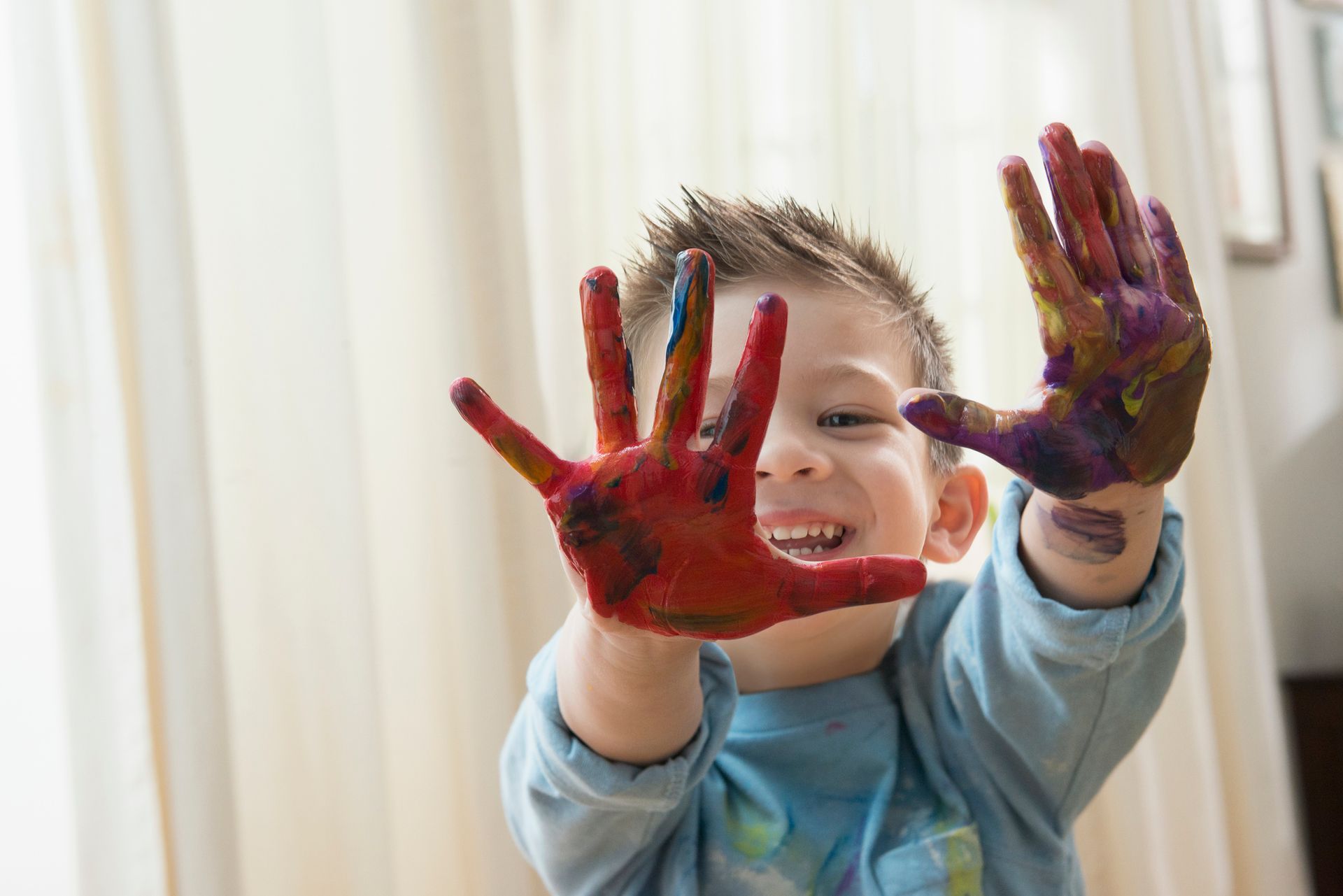 Boy with paint-covered hands smiles, holding them up.