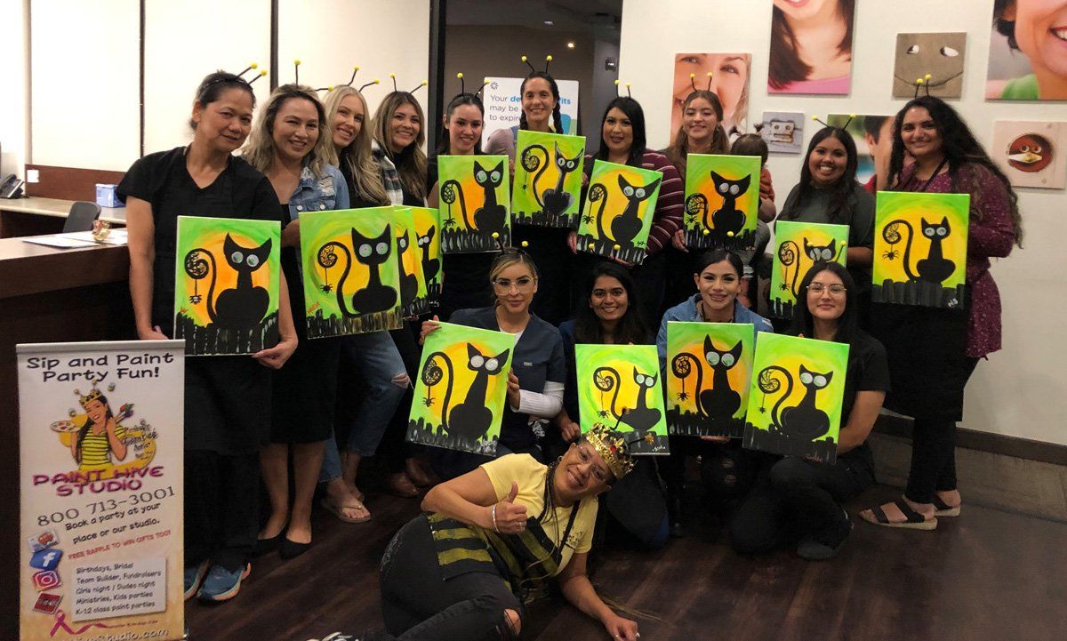Group of women holding Halloween cat paintings in a studio setting.