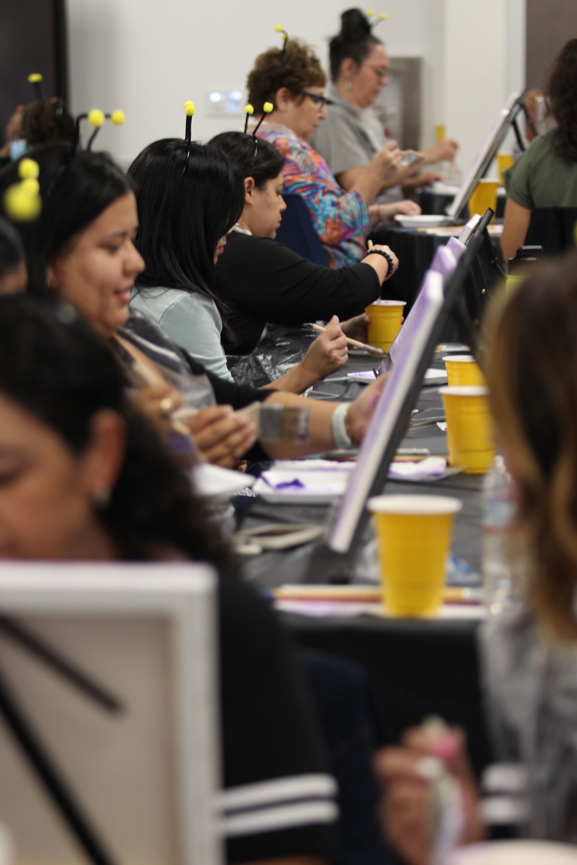 People painting at tables with canvases and yellow cups.
