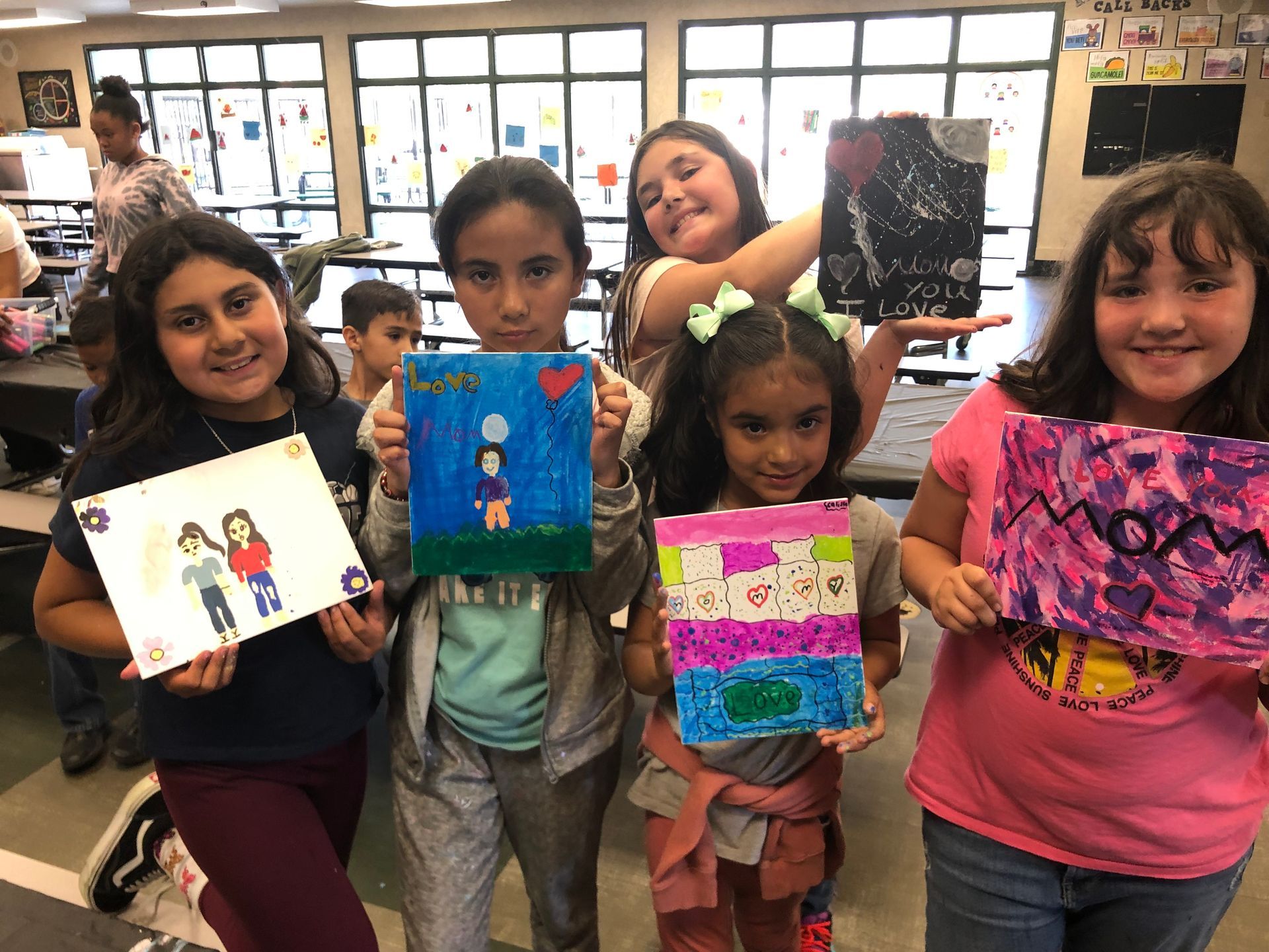 Group of children holding up colorful paintings in a brightly lit room.