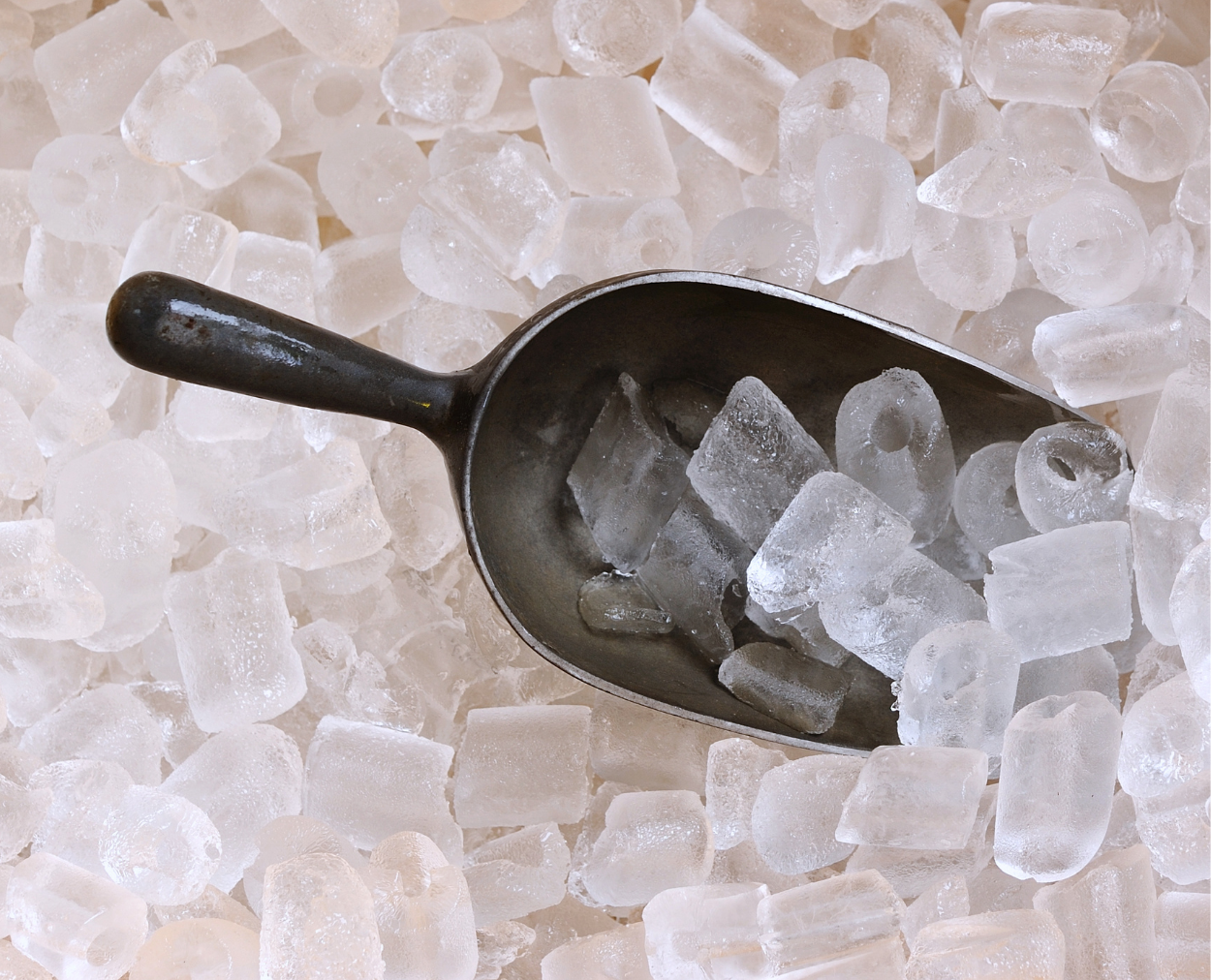 A metal scoop filled with ice cubes on a pile of ice