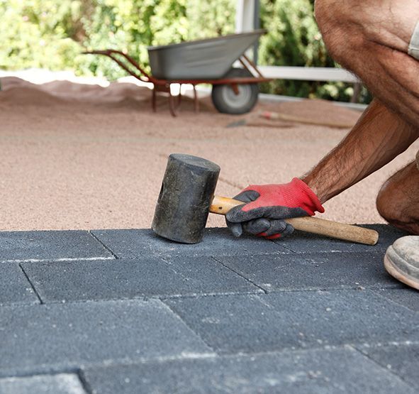 a man is kneeling down holding a hammer on a brick floor .