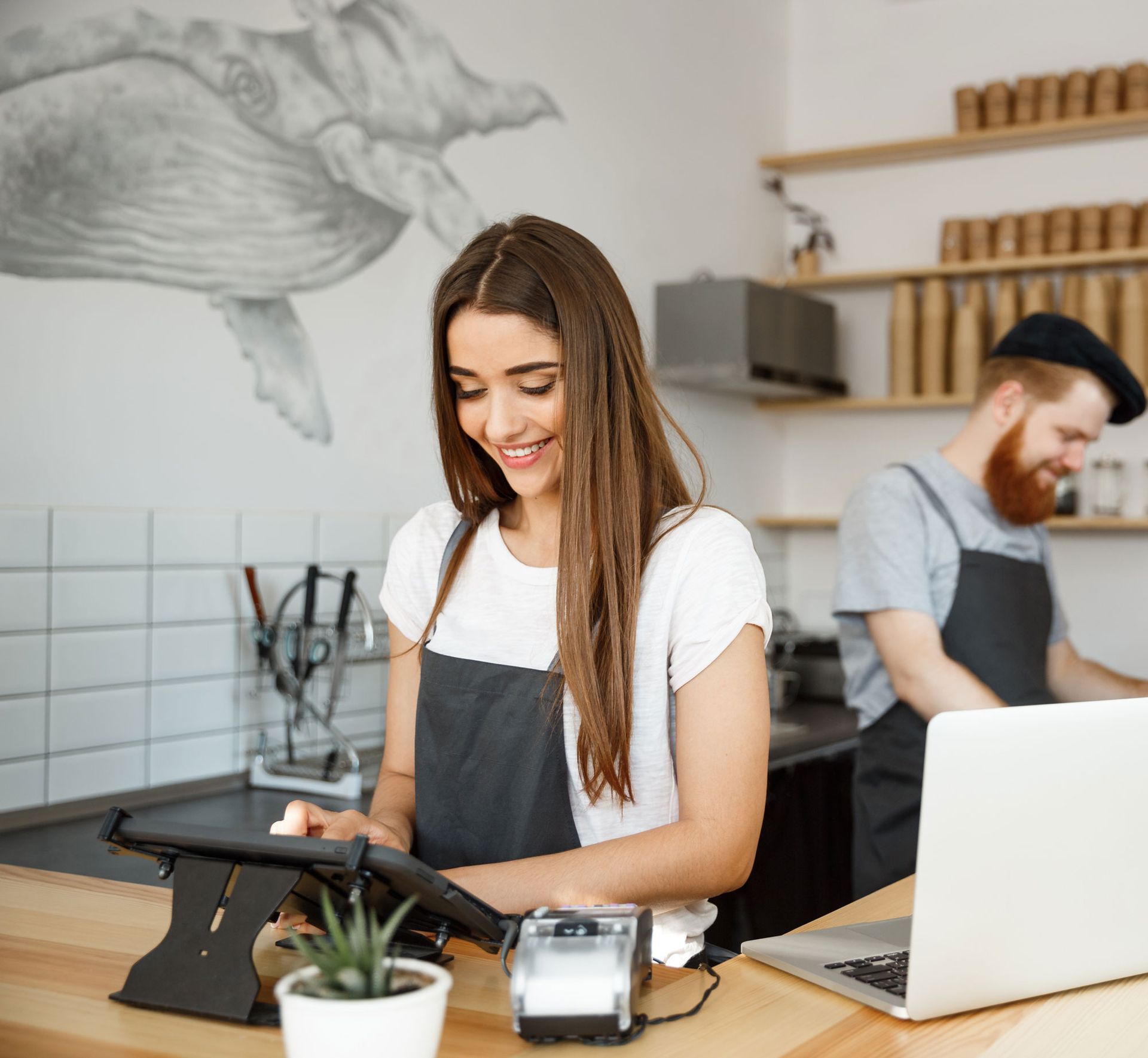 A woman is using a tablet while a man is using a laptop in a kitchen.