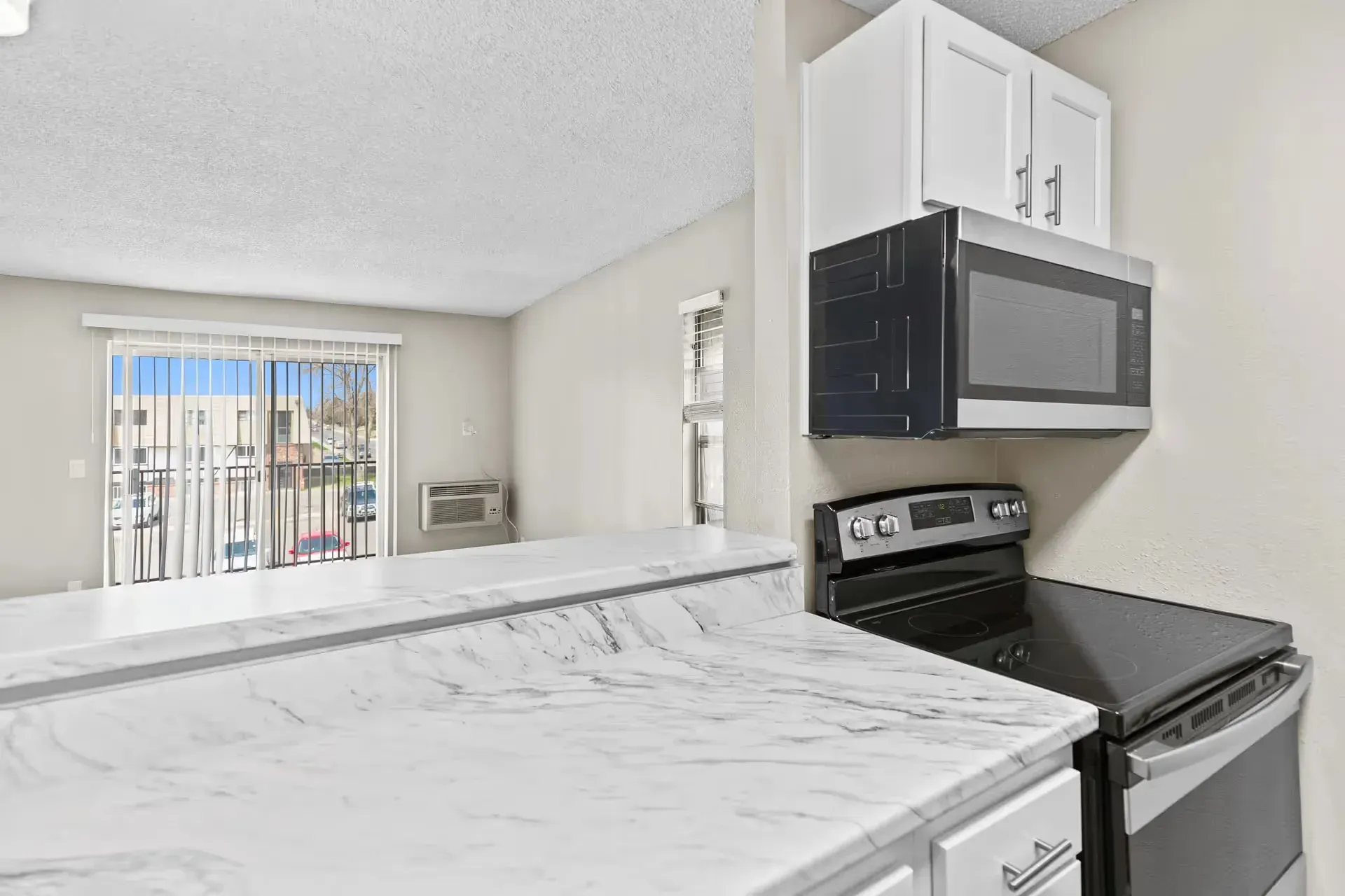 Kitchen in an apartment with marble countertops, white cabinets, microwave, and a stove at Avec Greeley.