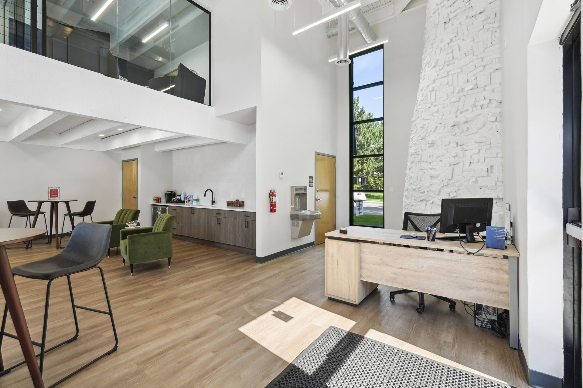 Modern office lobby with a reception desk, lounge seating, a kitchenette, and a high ceiling with tall windows at Avec Greeley.