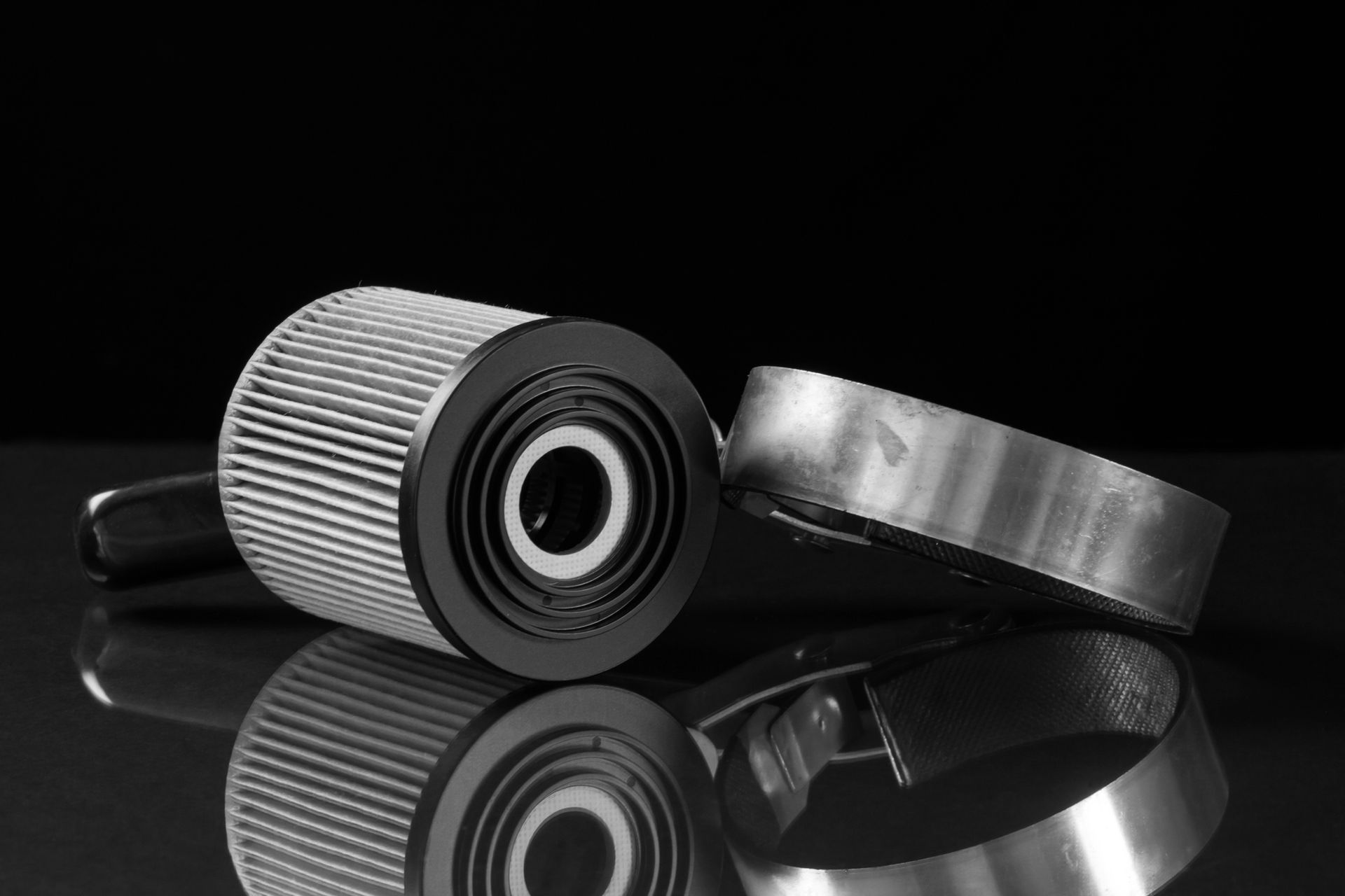 Filtro dell'olio e morsetto metallico su superficie riflettente.