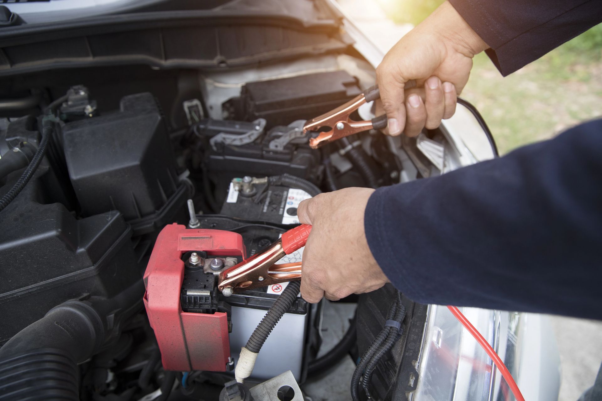 Mani che collegano i cavi di avviamento alla batteria di un'auto nel vano motore.