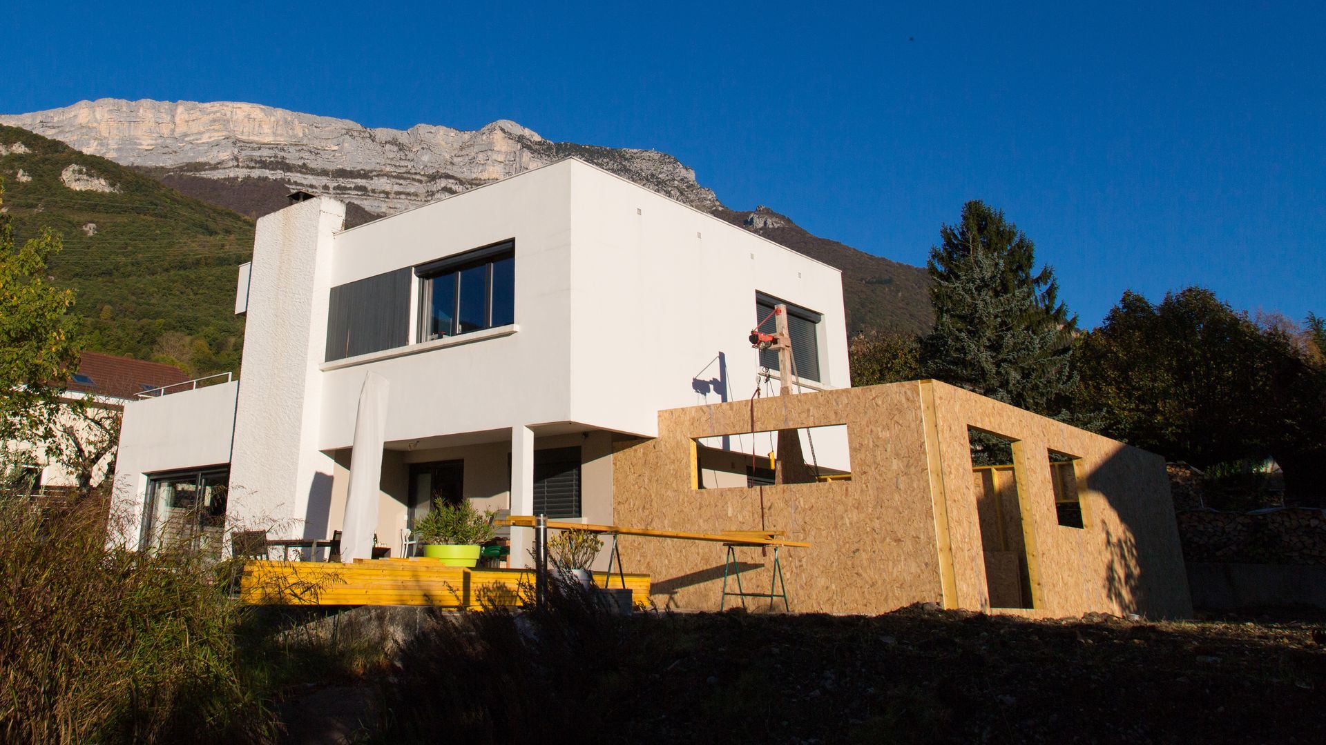 Maison blanche moderne avec une nouvelle structure en bois en construction, avec les montagnes en arrière-plan.